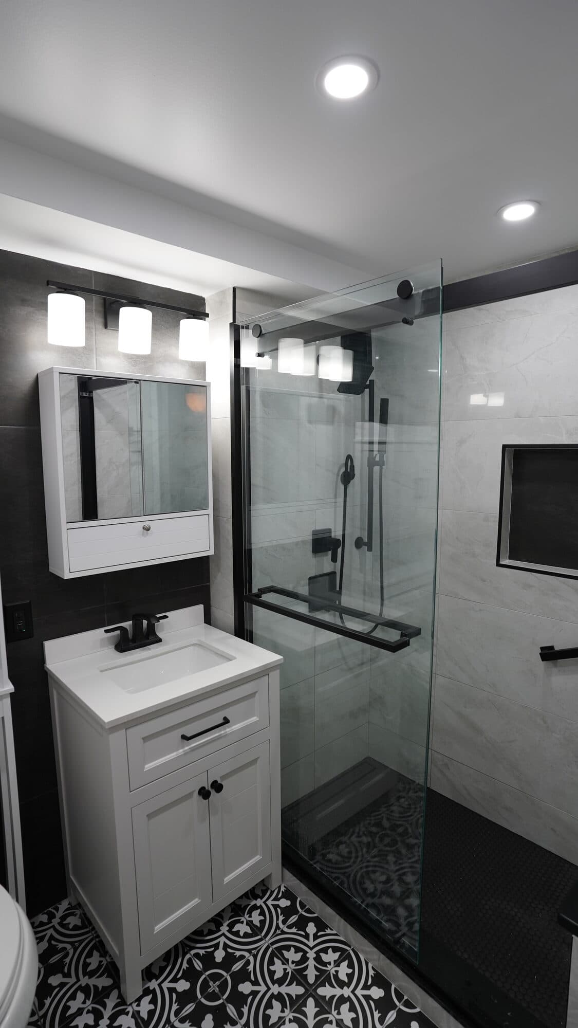 White vanity and lit medicine cabinet against dark tile in the Clinton Hill bathroom