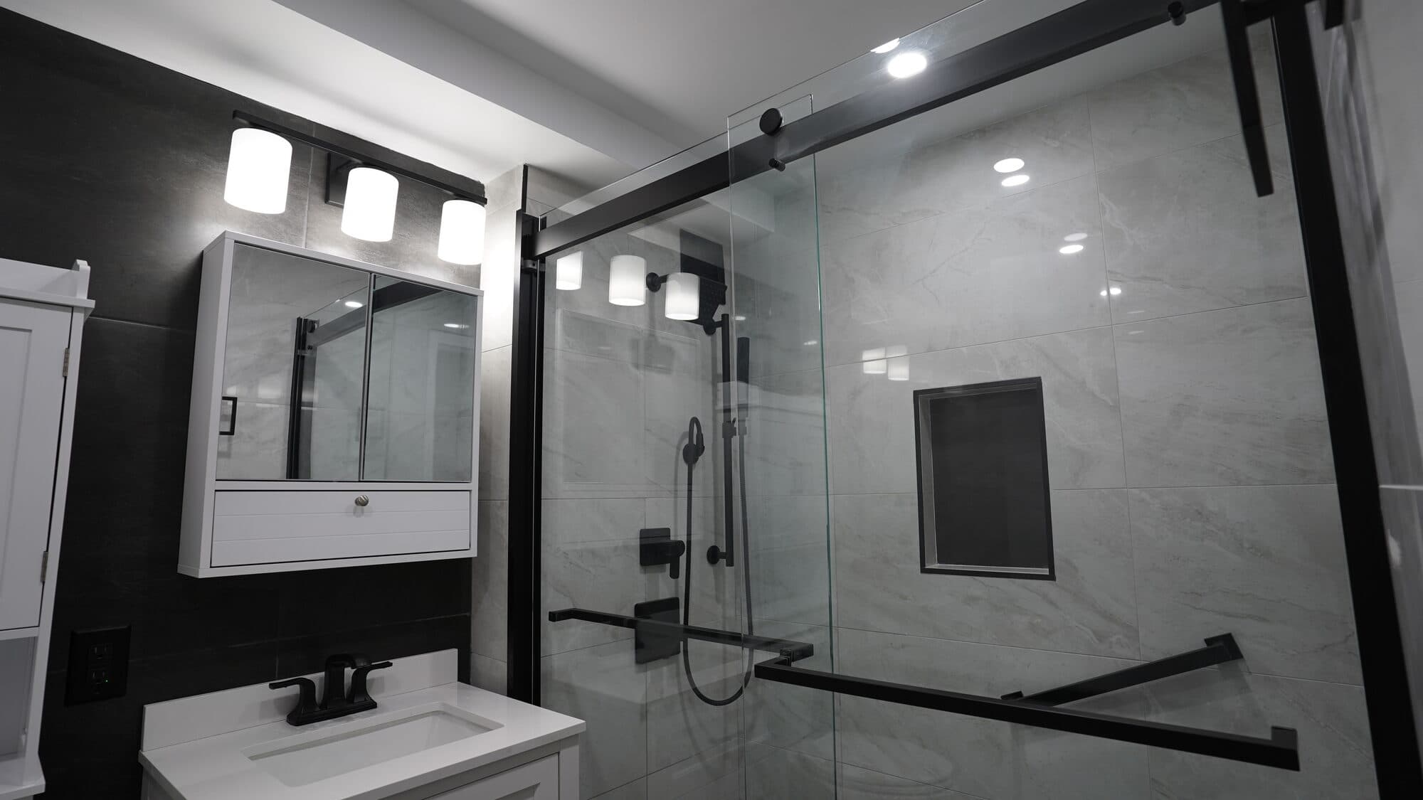 Medicine cabinet with sconce lighting beside the glass shower enclosure