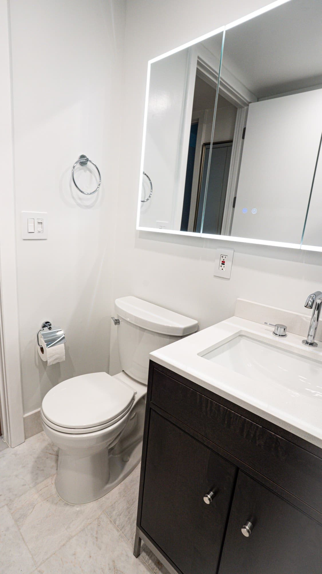 Dark-wood vanity and backlit LED mirror cabinet with chrome fixtures in the Dumbo condo bathroom