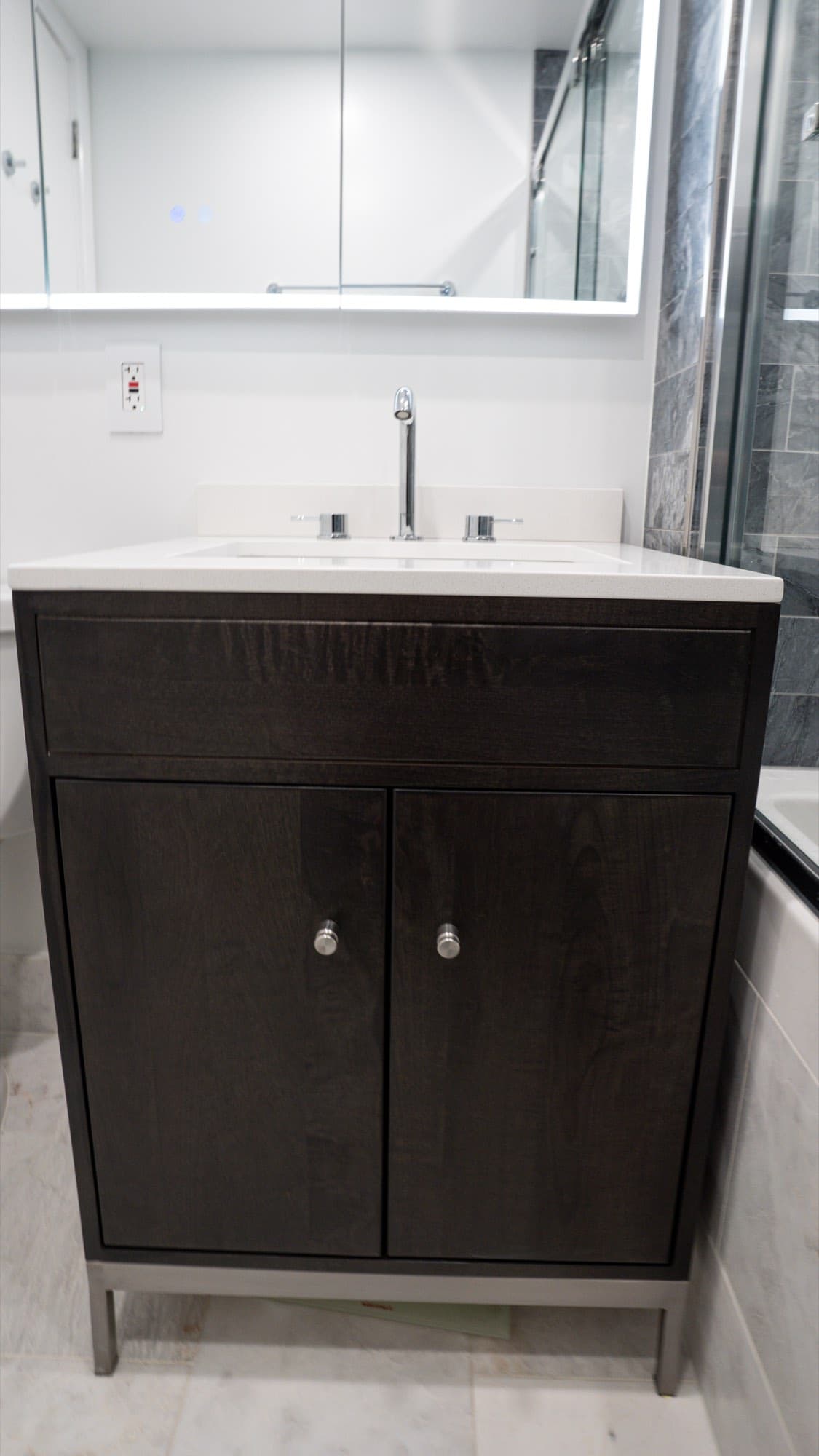 Dark-wood vanity with white top and chrome faucet on a marble-look tile floor