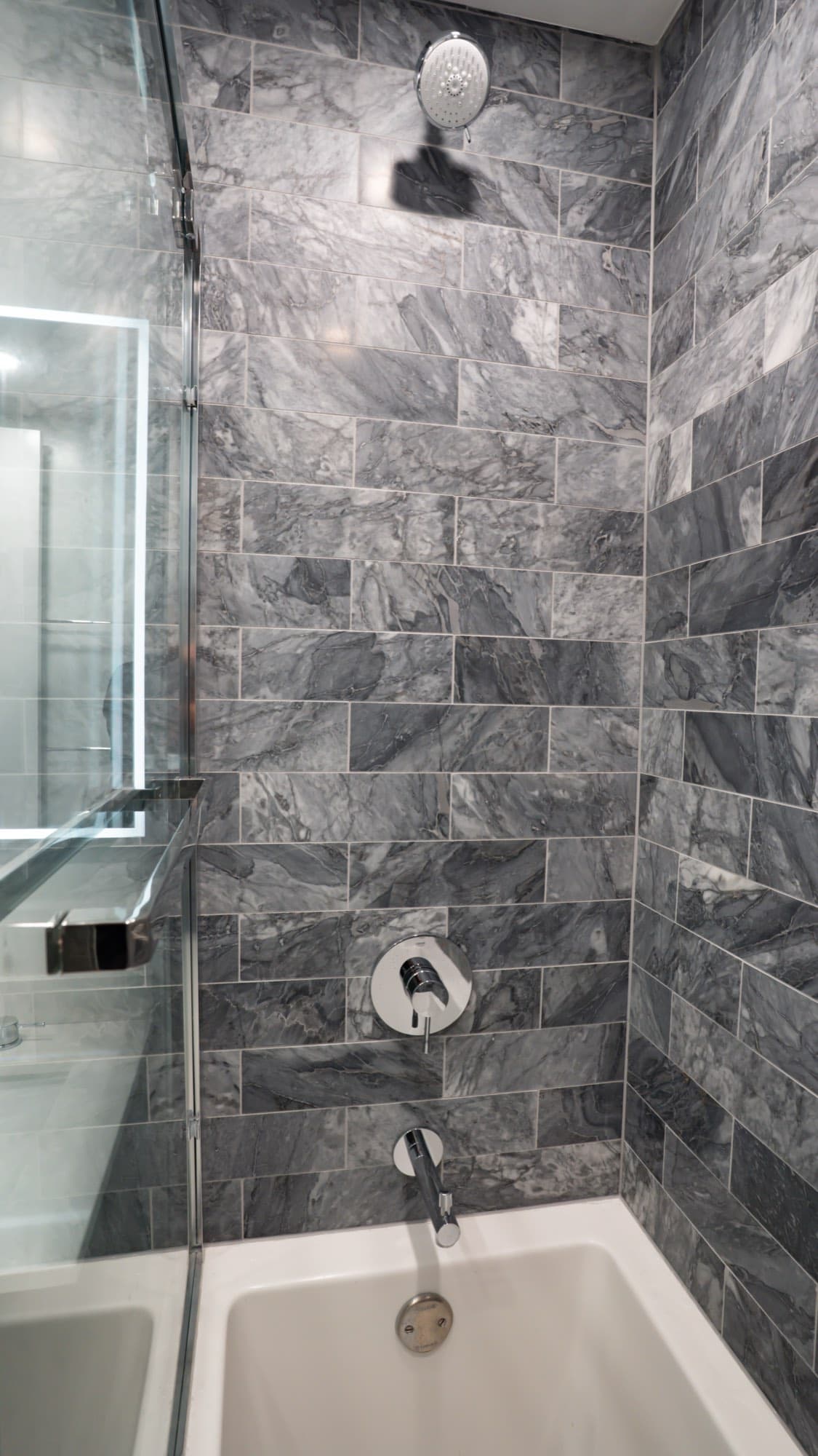 Gray stone-look tile tub and shower wall with chrome rain head and shower valve