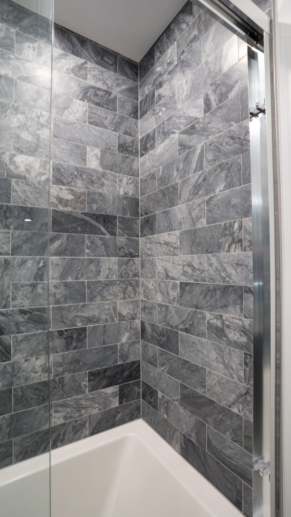 Corner detail of the gray stone-look tile running up the tub and shower surround