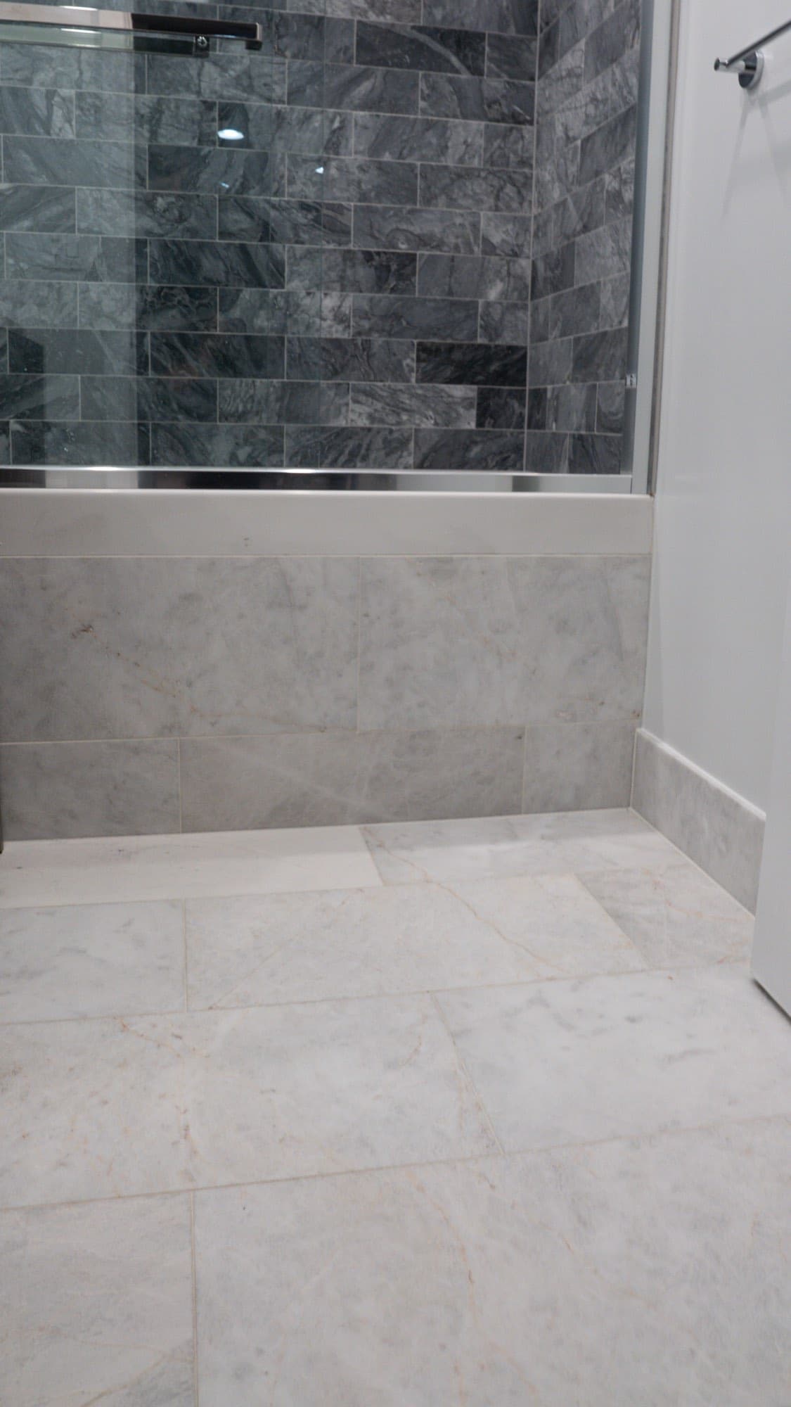 Light marble-look floor tile meeting the tiled tub apron below the glass enclosure